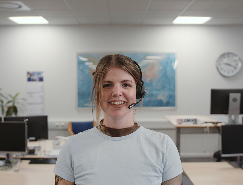 A young woman wearing a headset is smiling and standing in the office