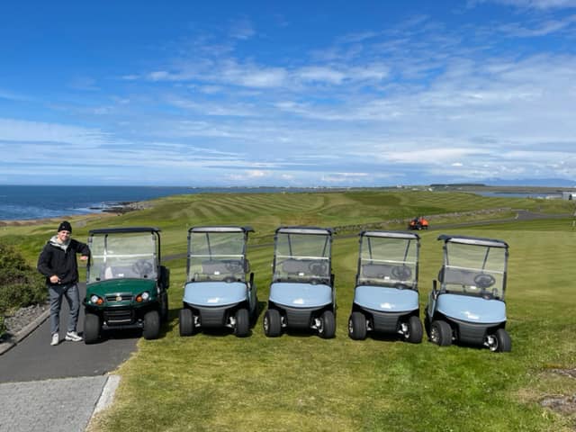 Man is standing with a green golf cart with sea in the background