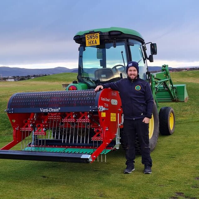 Man working at HÁ Verslun is standing with a golf course mower on a green field 